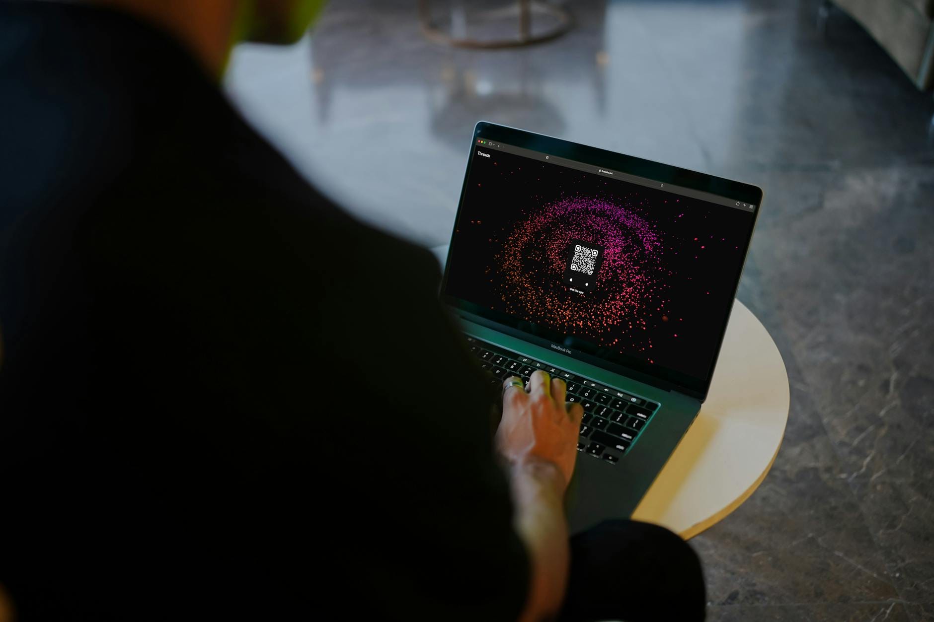 Osoba skanuje kolorowy kod QR na ekranie laptopa w przestrzeni coworkingowej