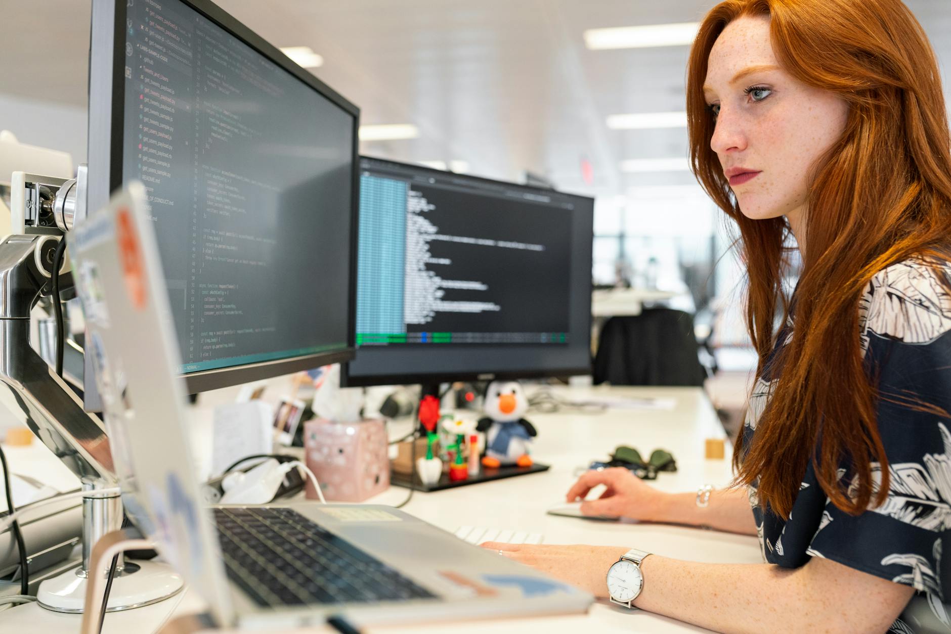 Programistka pracuje nad kodem na dwóch monitorach w nowoczesnym biurze