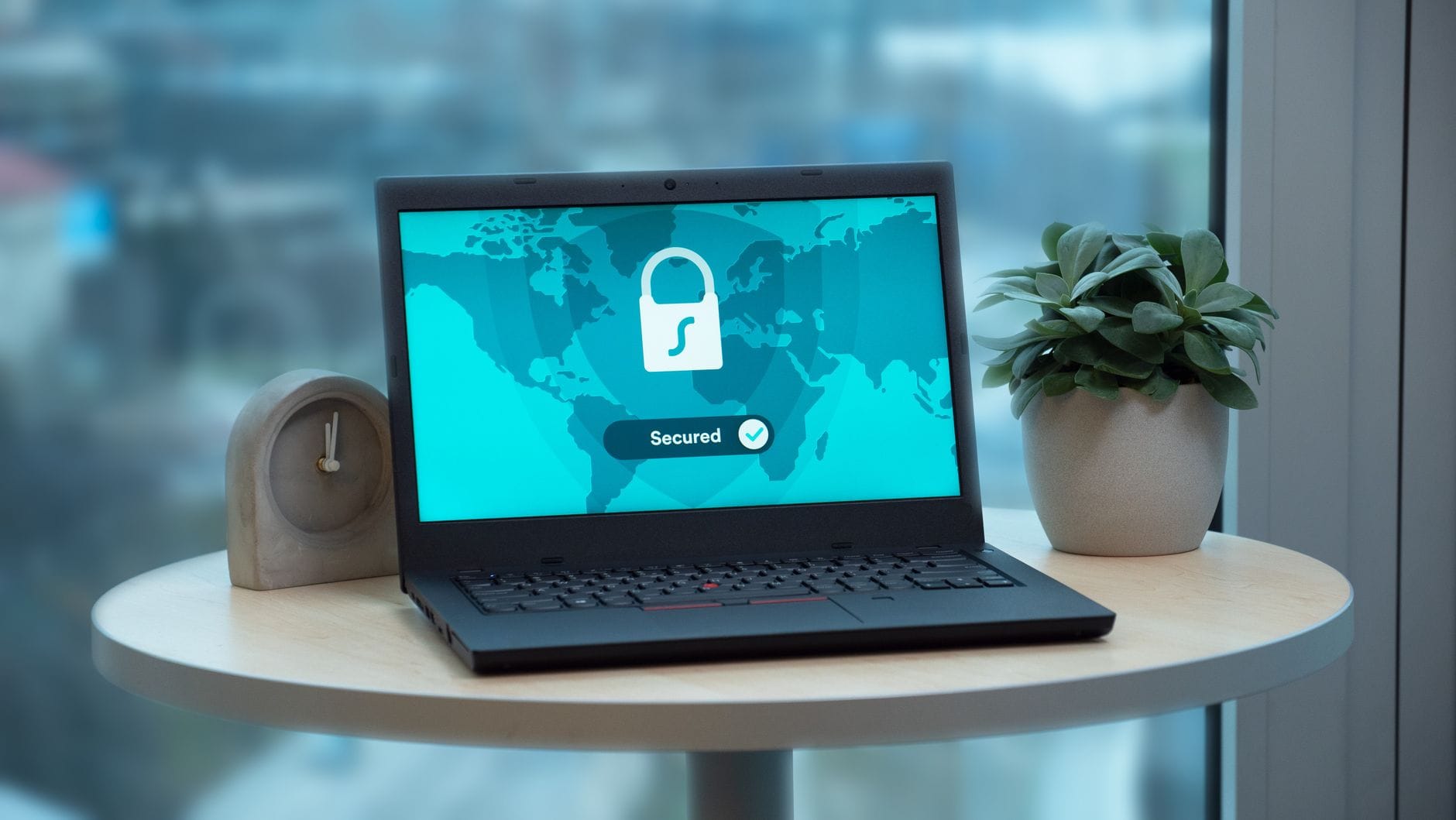 Laptop z ikoną kłódki na stole obok rośliny i zegara